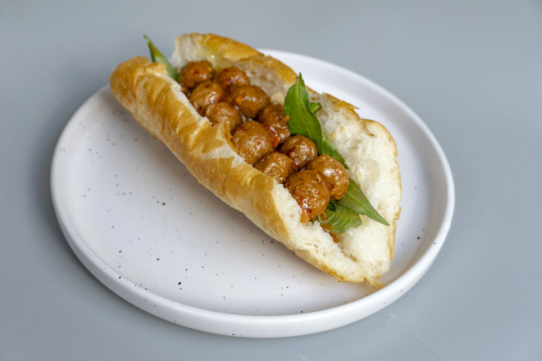 A num pang baguette sandwich filled with meat and fresh herbs on a plate