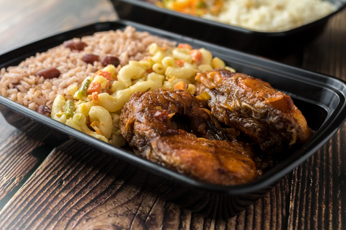A takeaway tray of stewed meat with rice and peas and macaroni