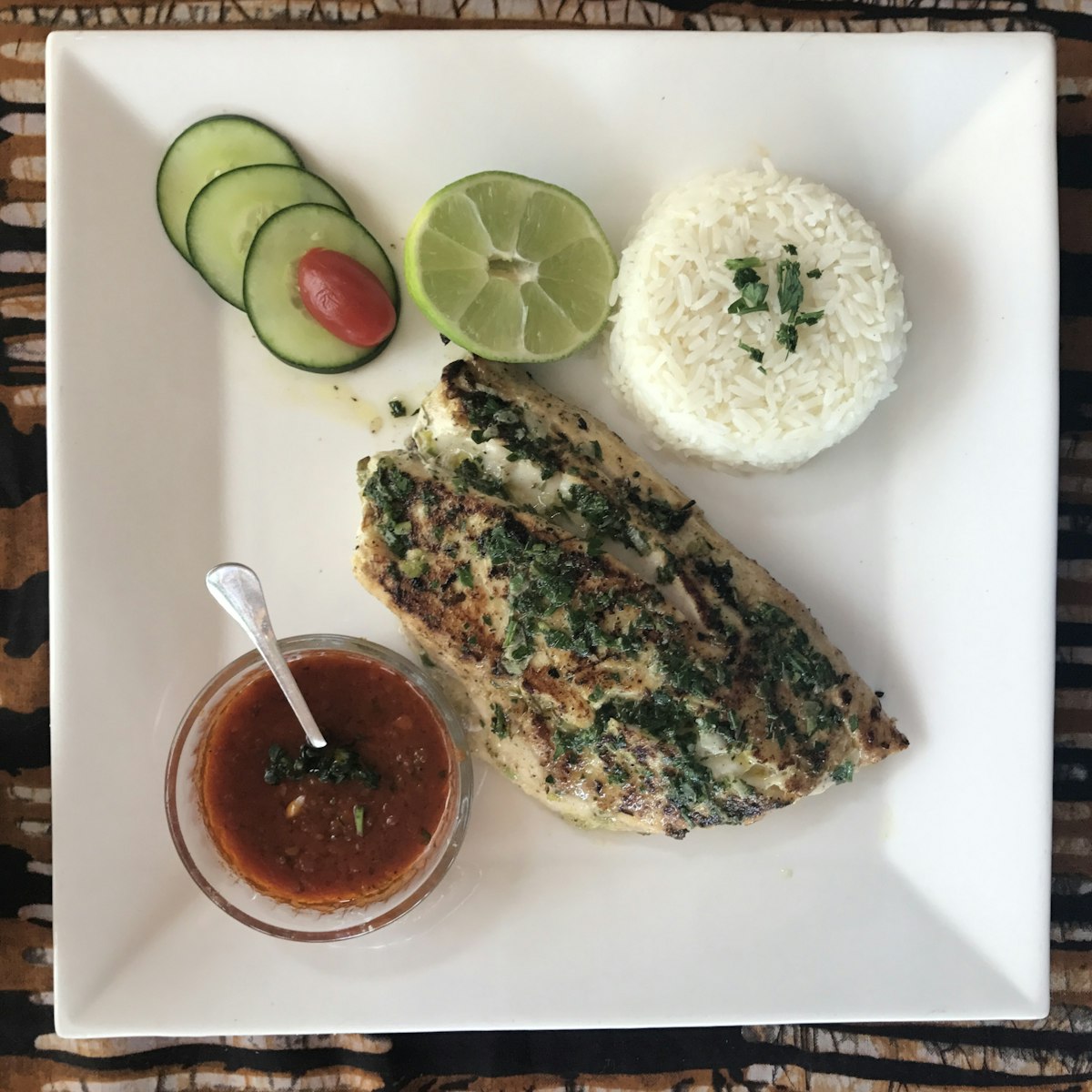 A cooked fish fillet in sauce served with rice and a bowl of gravy