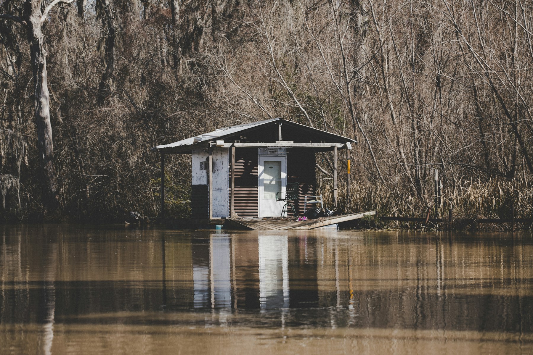 A stilted fishing camp standing over brown bayou water in the Louisiana swamp