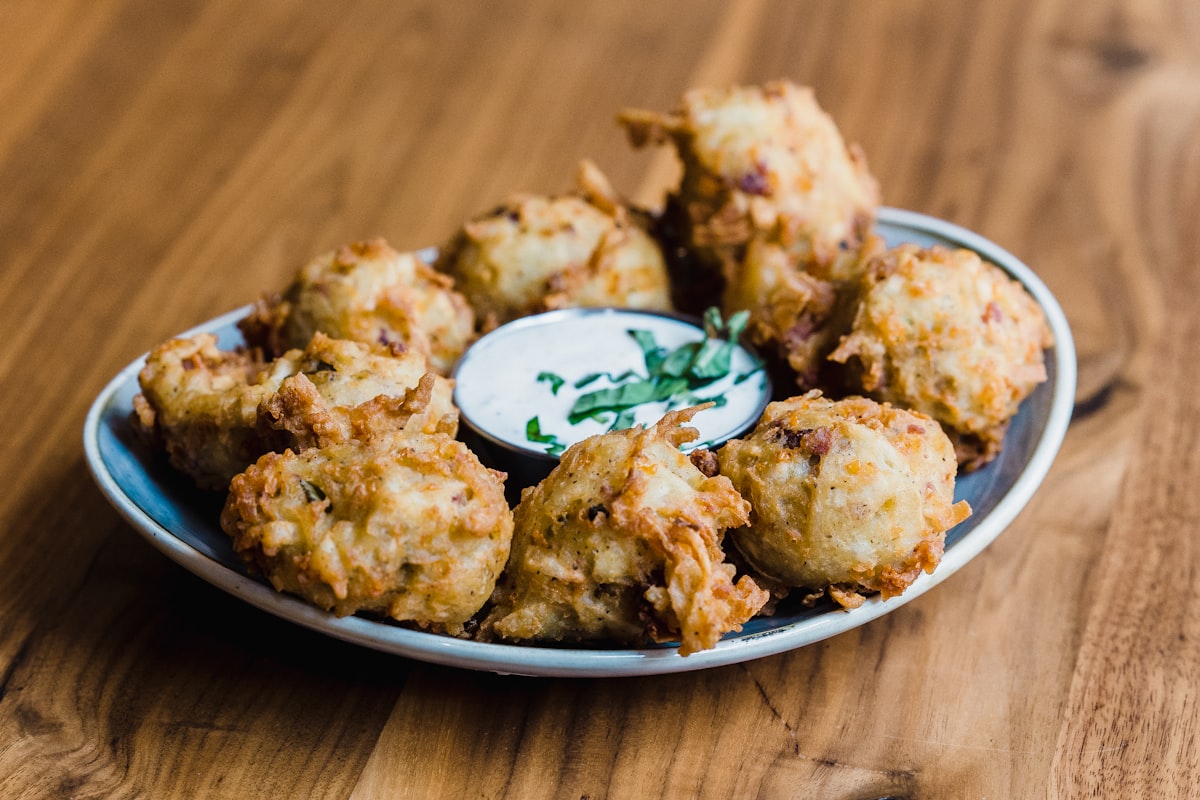 Small golden fried fritters served on a plate with a dipping sauce