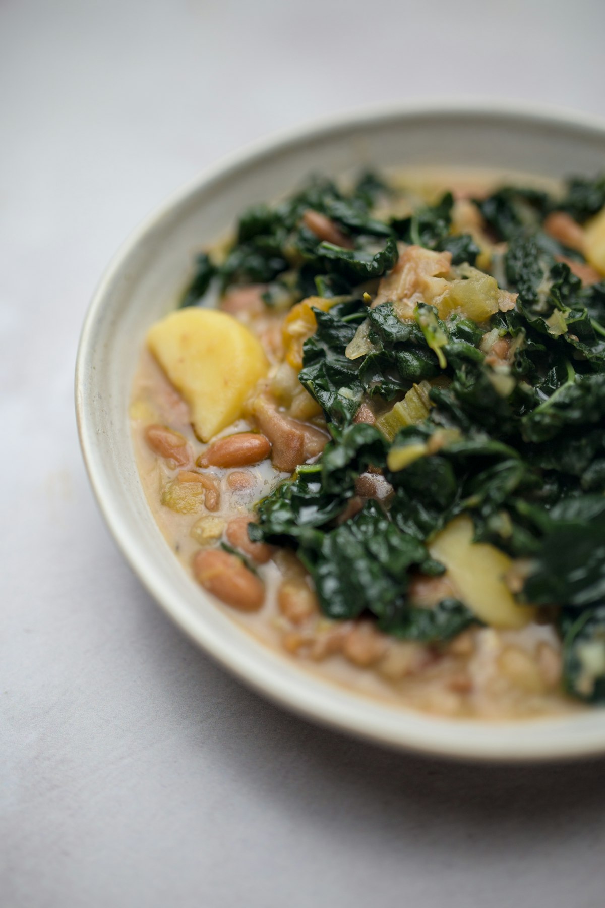 A creamy soup of dark leafy greens with potato and beans in a shallow bowl