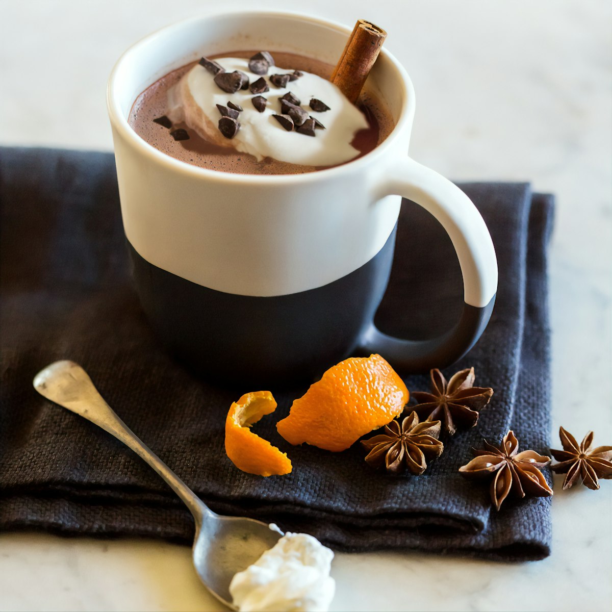 A mug of thick dark hot chocolate with star anise and orange peel beside it