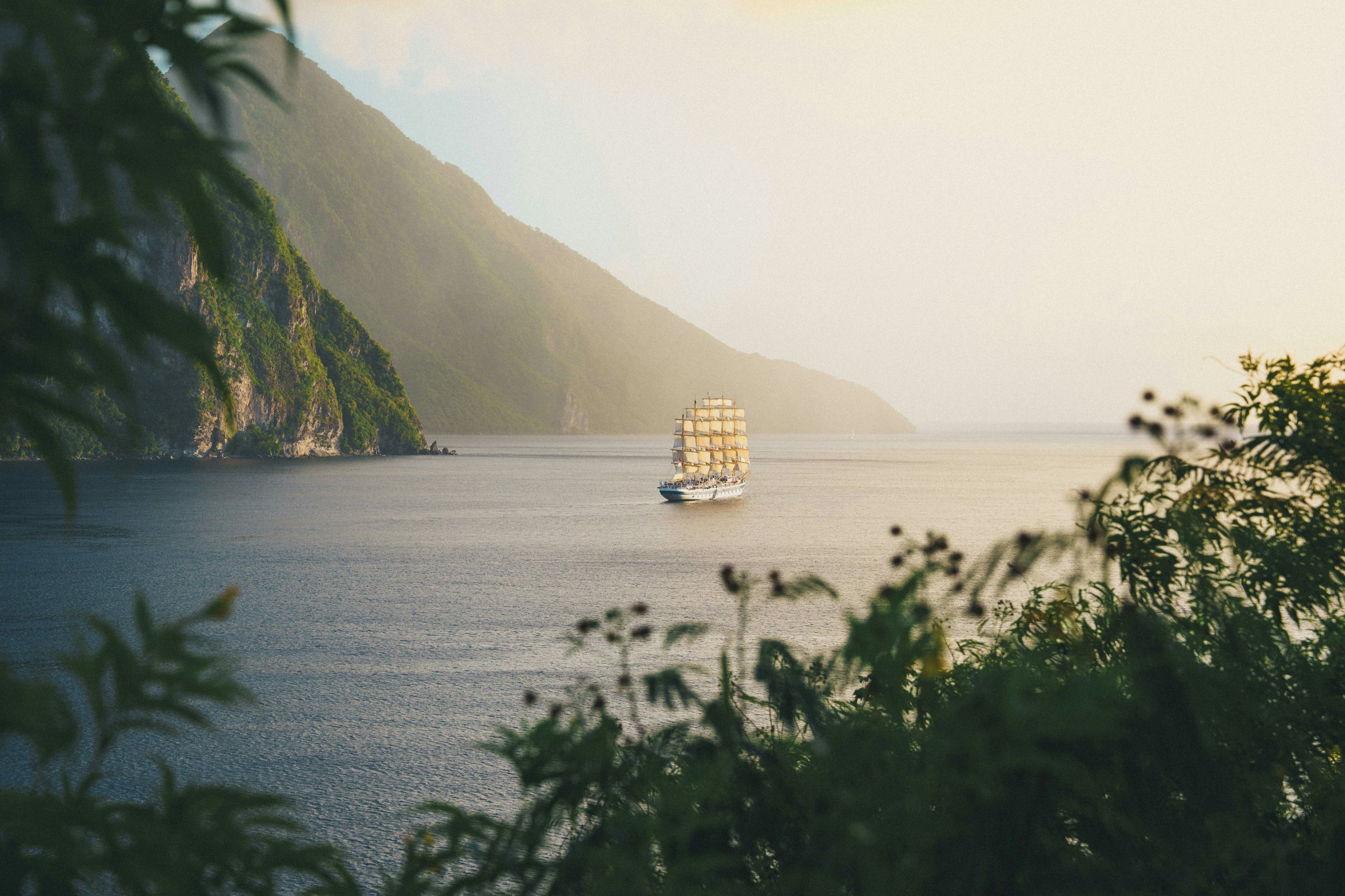 A sailing boat on calm water below the steep green cliffs of Saint Lucia