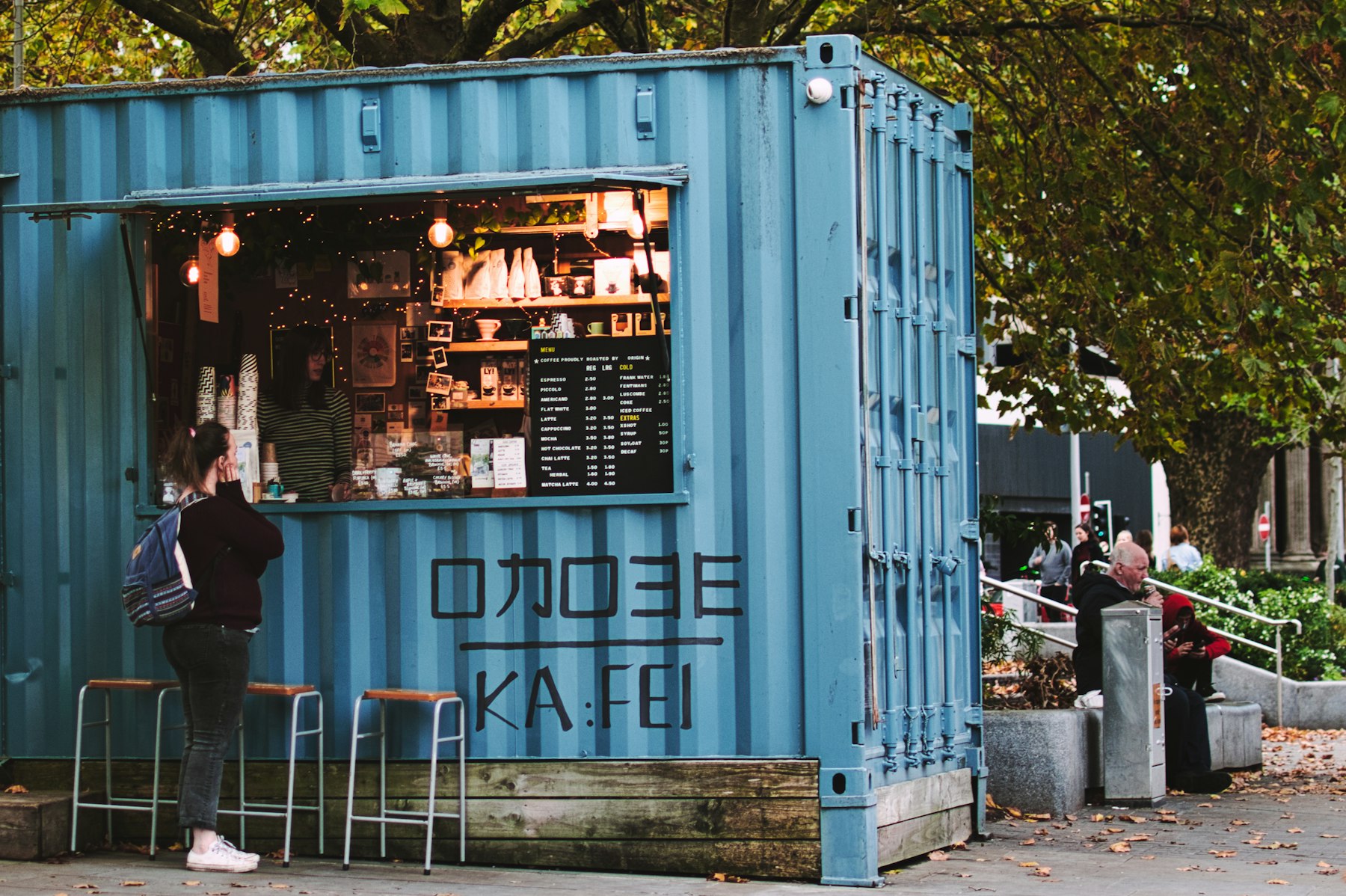 A shipping container converted into a small cafe with people standing at the counter