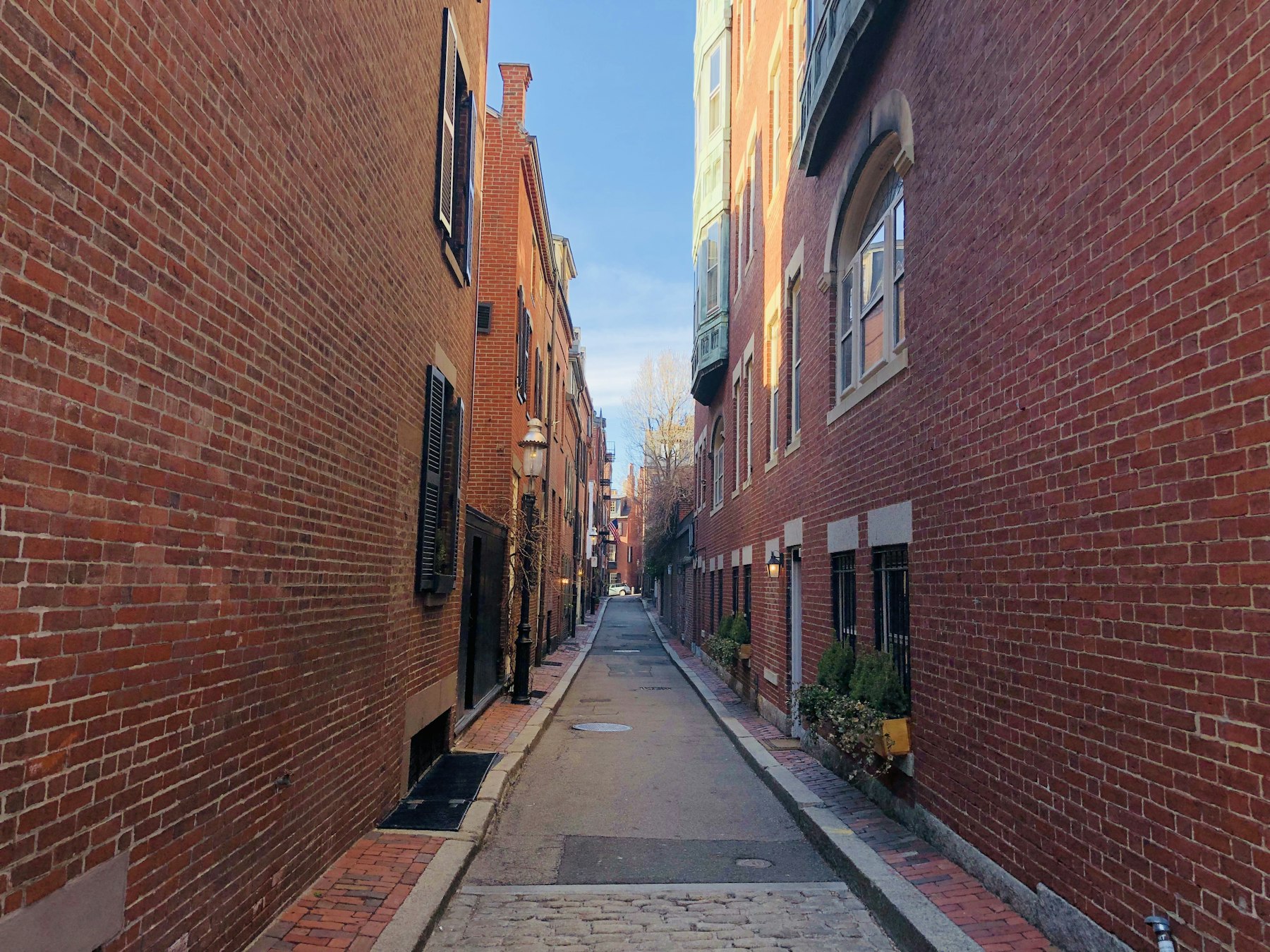 A narrow brick lane between old brick row houses in Boston on a bright day