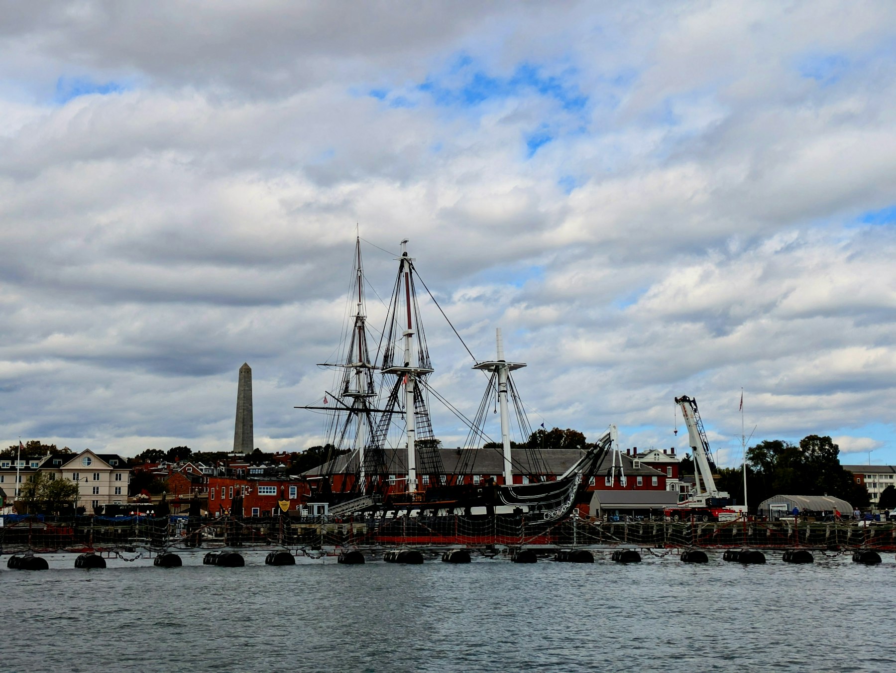 The USS Constitution moored at Charlestown Navy Yard with the Bunker Hill Monument obelisk behind