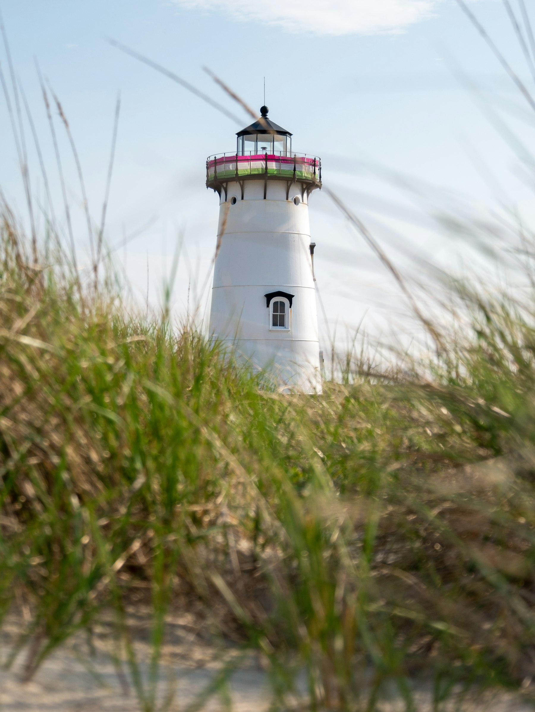 A white lighthouse on Cape Cod seen behind tall beach grass under a blue sky
