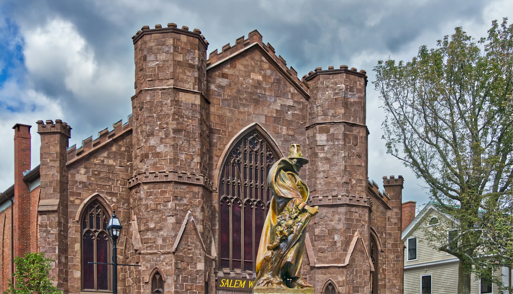 The stone gothic facade of the Salem Witch Museum with the bronze Roger Conant statue in front