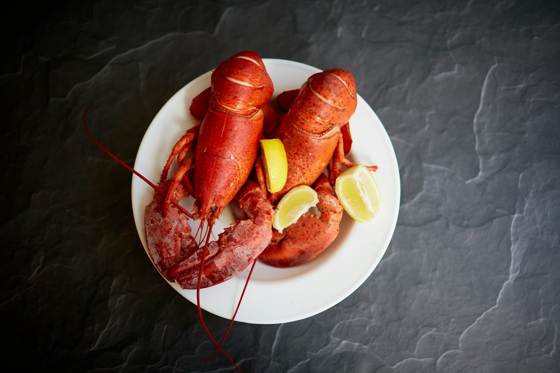 Two whole steamed red lobsters with lemon wedges on a white plate