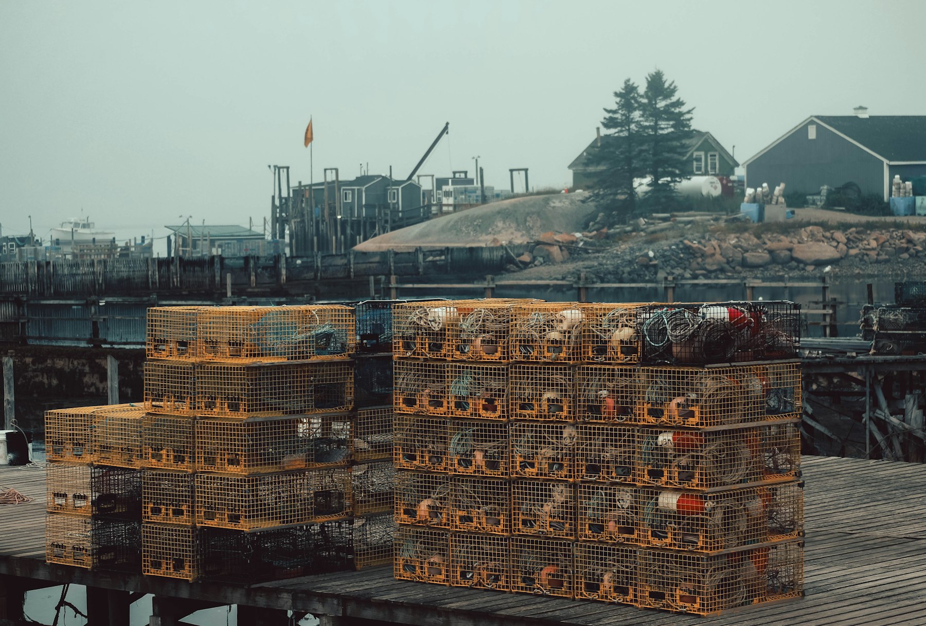 Stacked lobster traps and fishing gear on a working wharf beside a shingled fish house in Maine