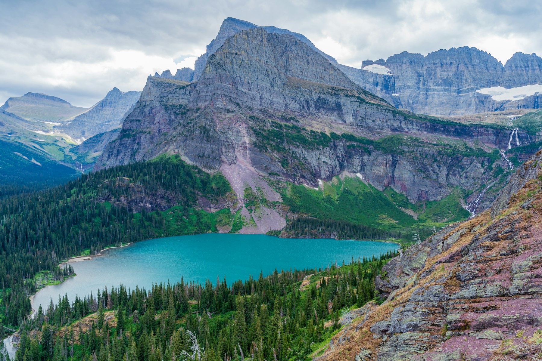 A turquoise glacial lake below a grey rock wall in the Many Glacier area of Montana