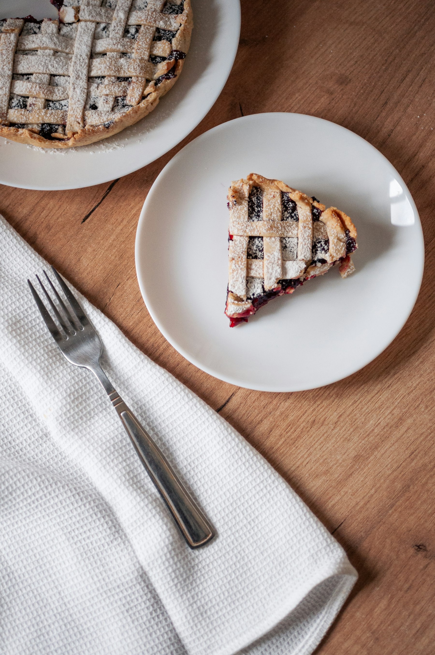 A slice of dark berry pie with a lattice crust on a white plate beside a fork