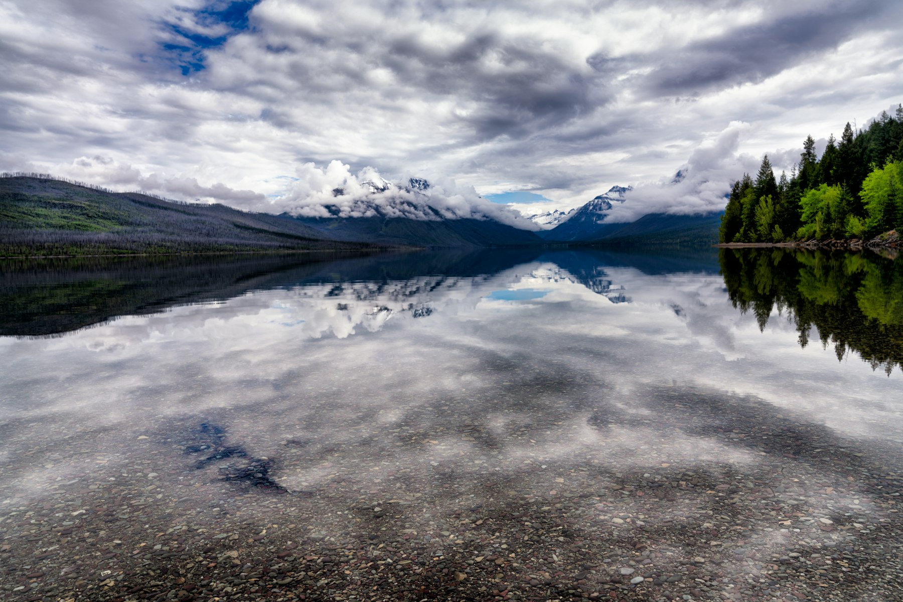 Cloud and snowy peaks mirrored in a still lake in Glacier National Park Montana