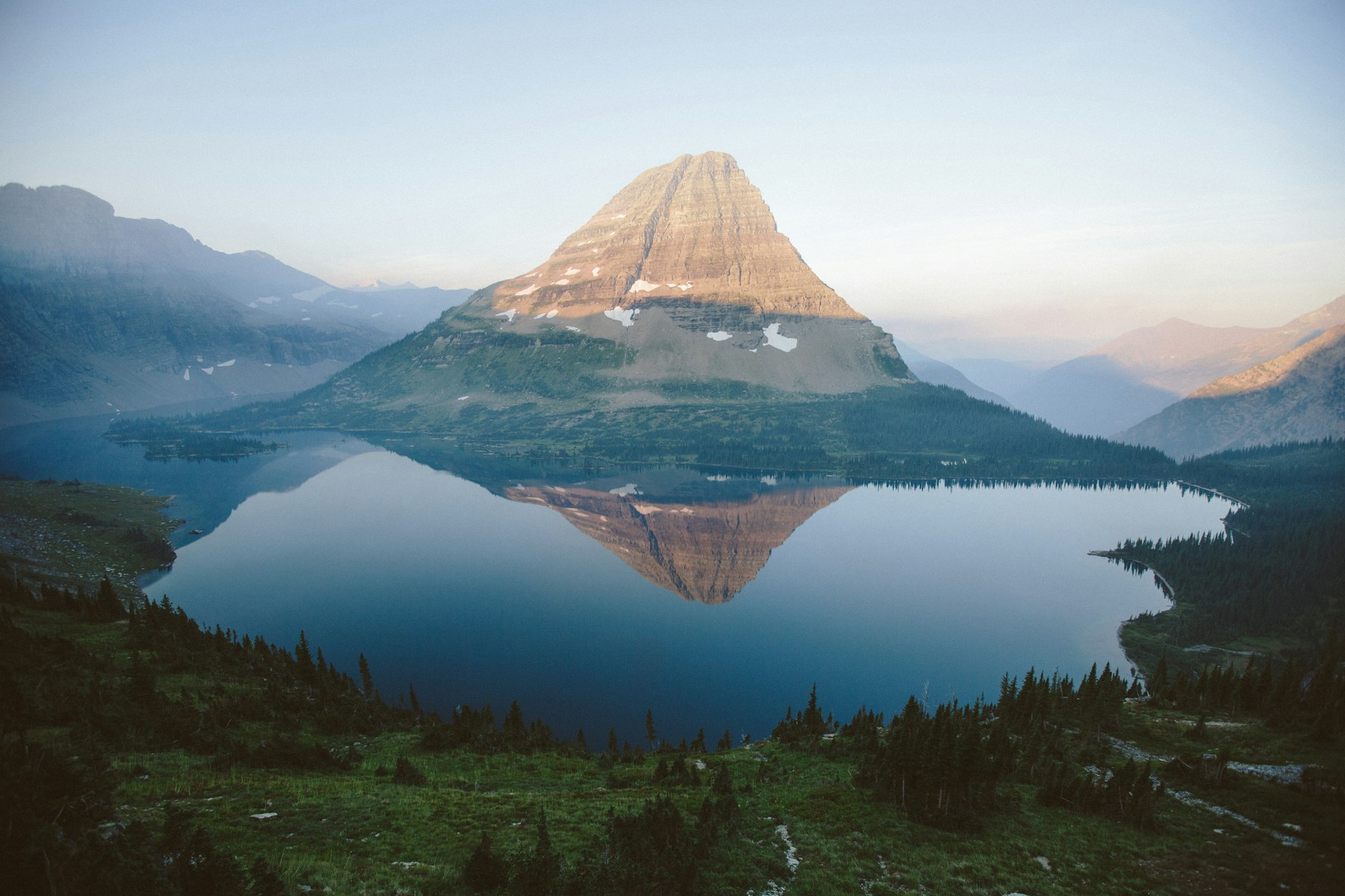A pyramid shaped peak reflected in a still alpine lake at Logan Pass in Glacier National Park