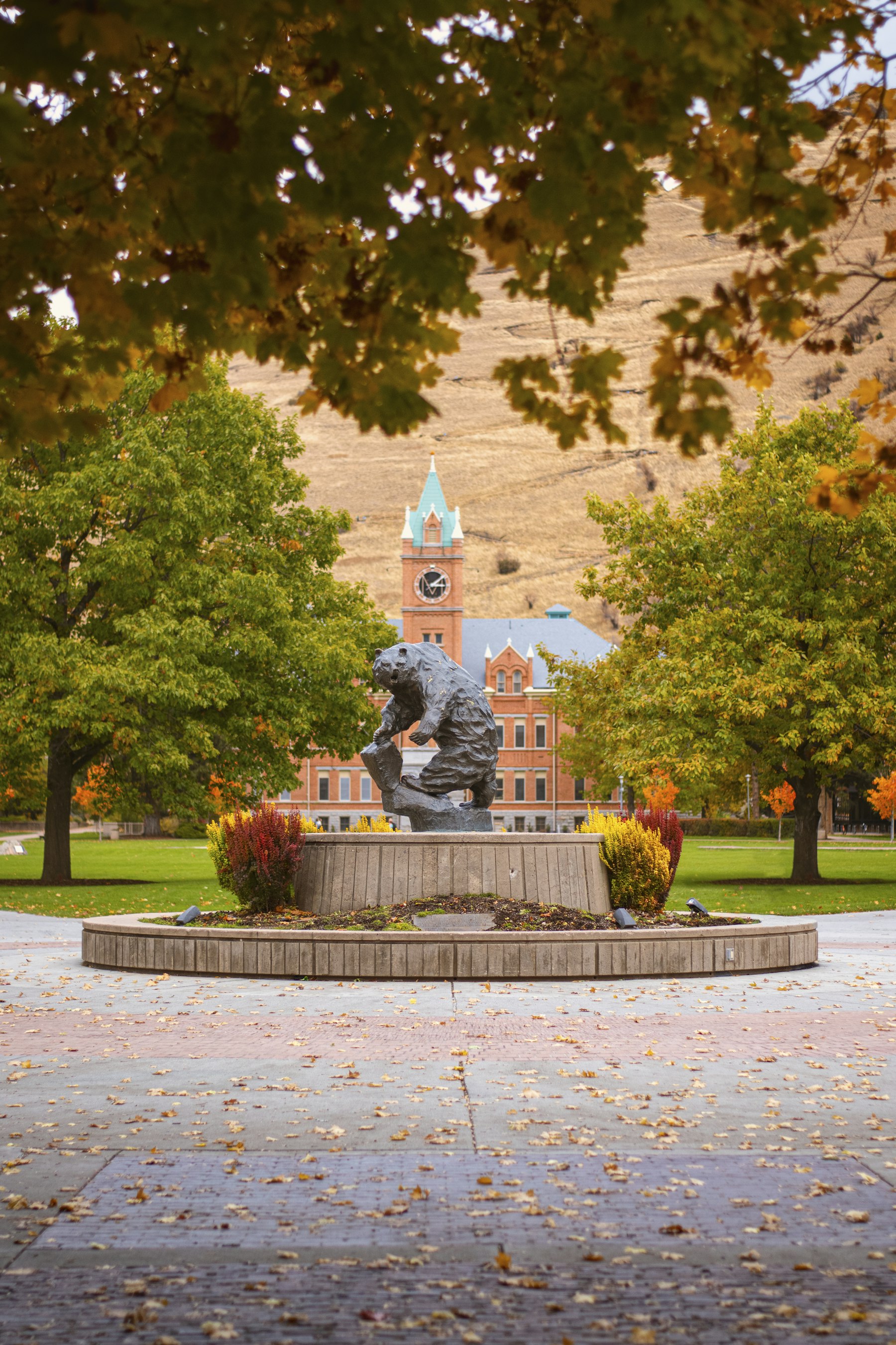 A statue and fountain in a downtown park with a clock tower behind in Missoula Montana