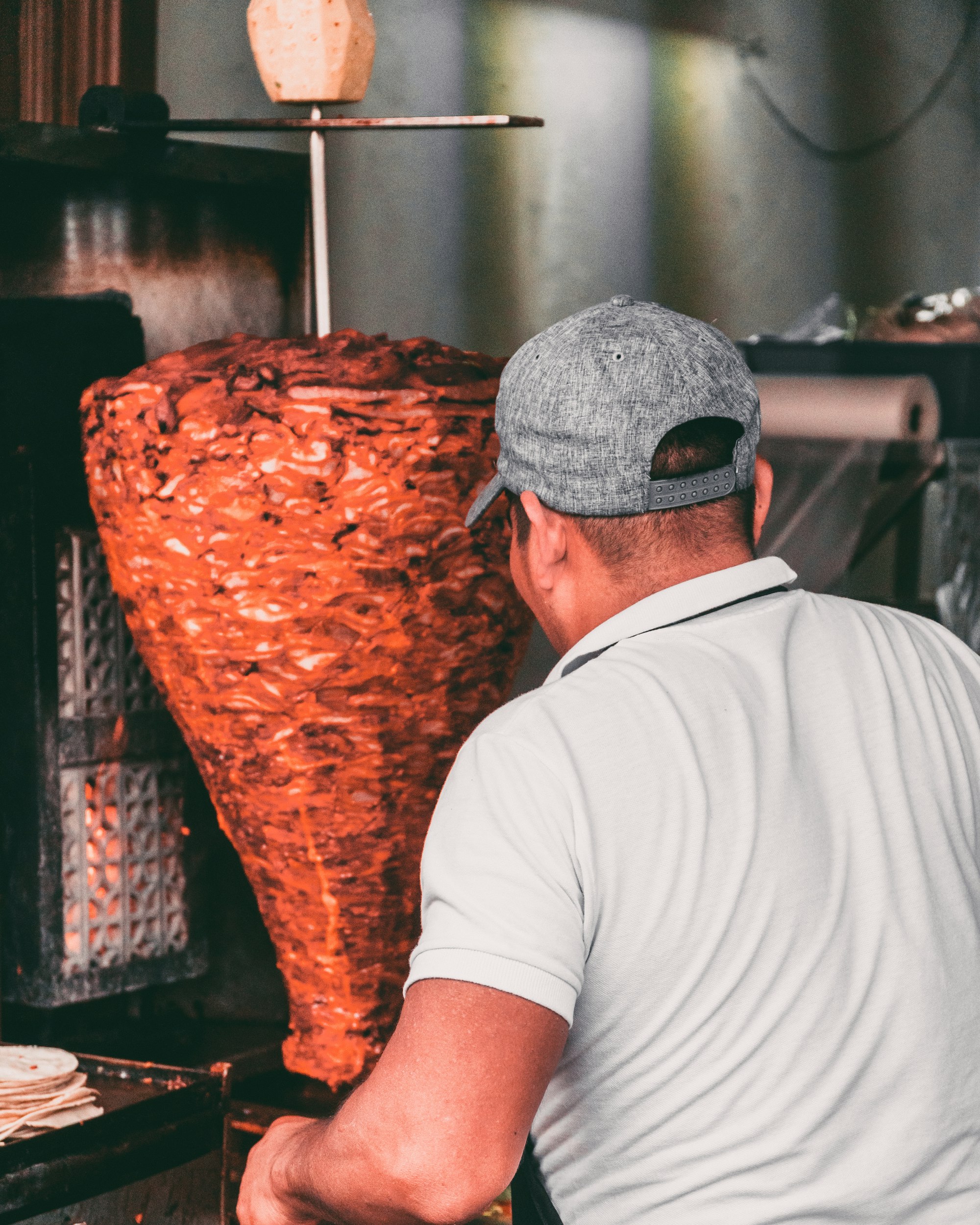 A taquero carving pork from a vertical al pastor trompo at a Mexican street stand