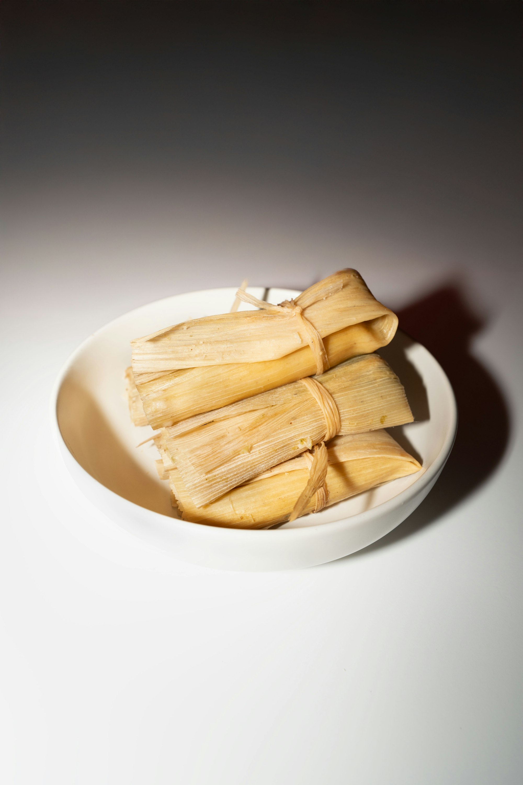 Tamales wrapped in corn husks stacked on a white plate
