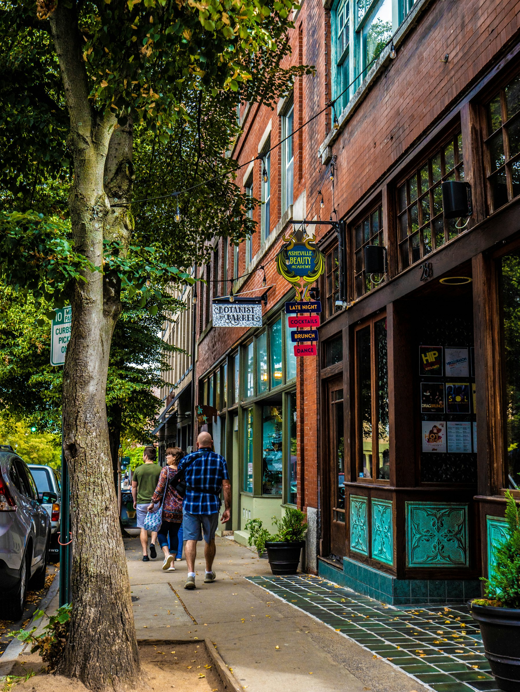 A tree lined street of brick storefronts in downtown Asheville North Carolina with people walking