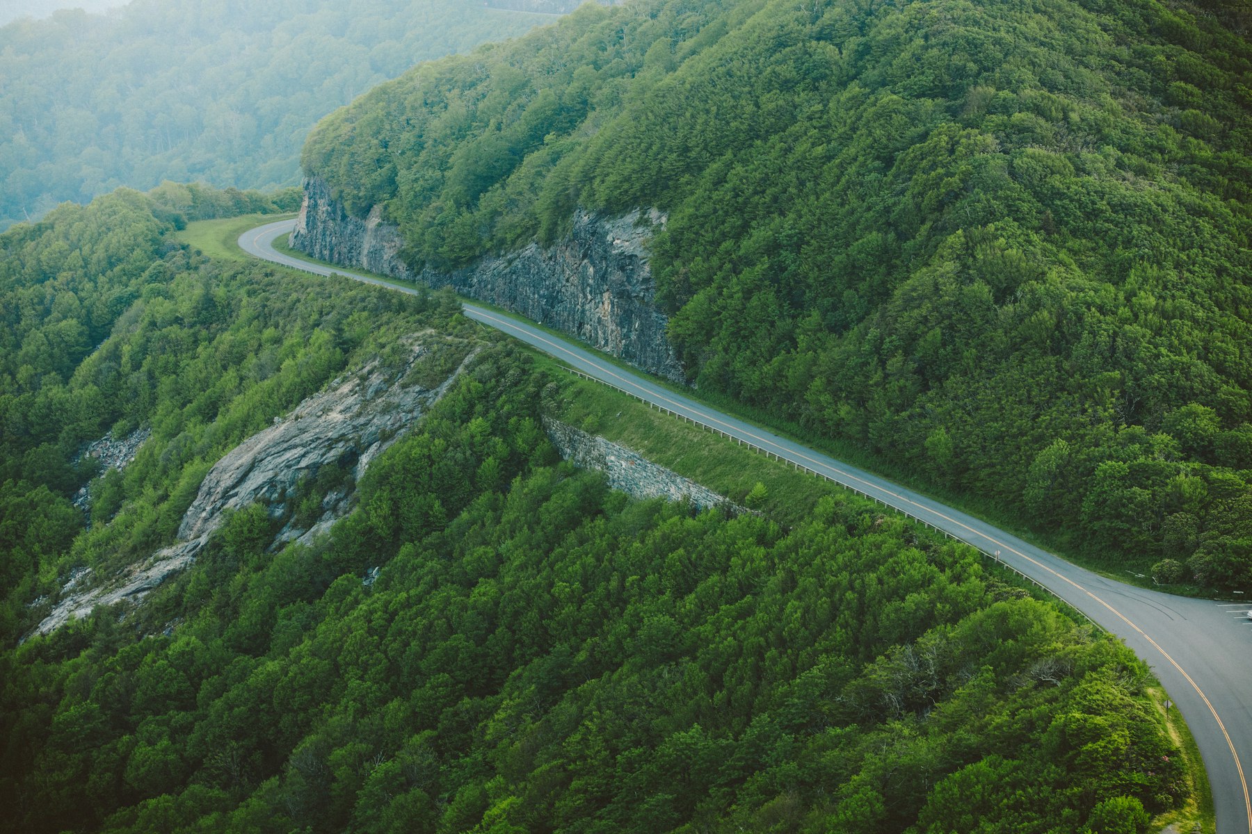 A two lane road curving along a steep forested mountainside in the North Carolina Blue Ridge