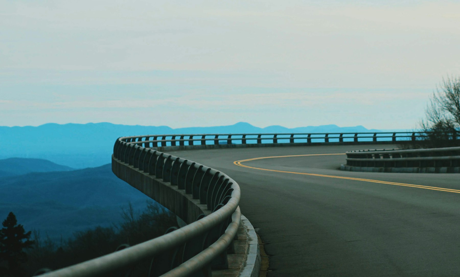 A curving guardrailed mountain road with layered blue ridges in the distance on the Blue Ridge Parkway