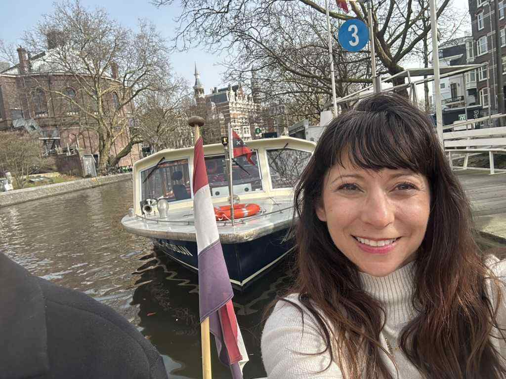 A small canal cruise boat moored on an Amsterdam canal with bare trees along the water