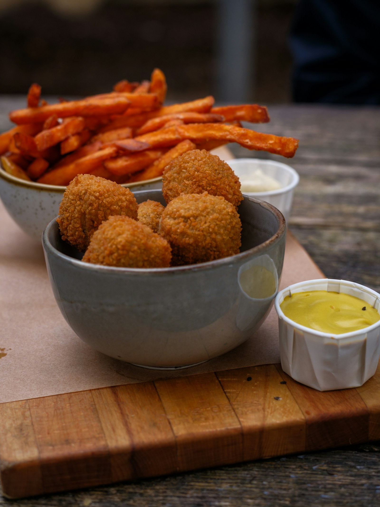 A bowl of golden fried bitterballen with mustard and fries beside it