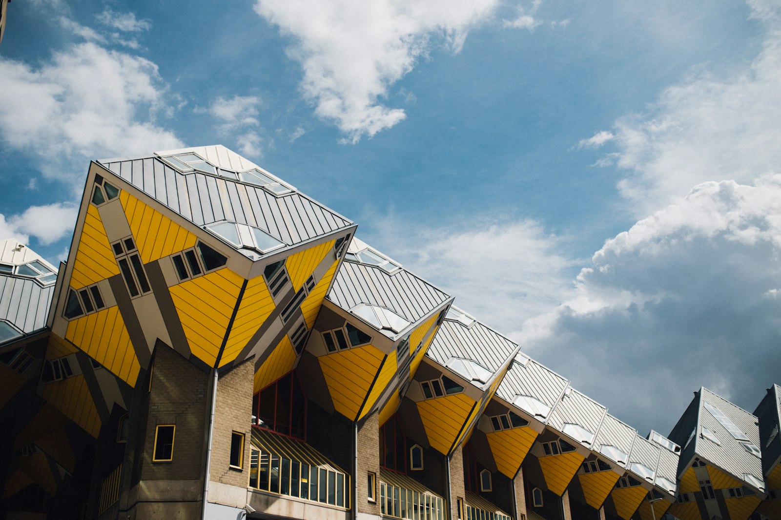 The yellow tilted Cube Houses of Rotterdam against a blue sky with cloud