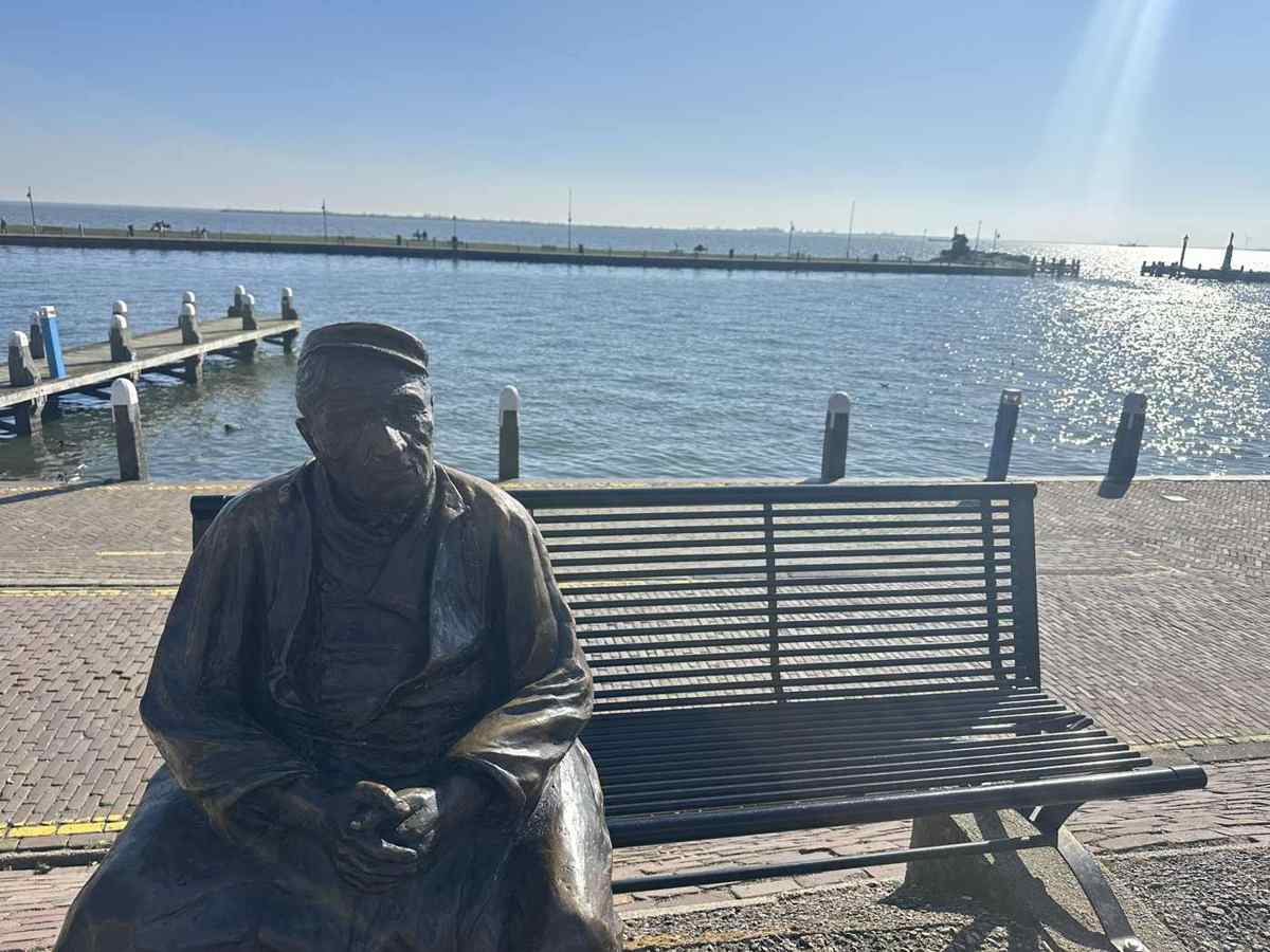 A bronze statue of a seated fisherman on a bench looking out over the water at Volendam harbour