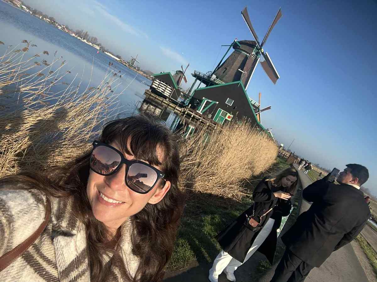 A working wooden windmill on the water at Zaanse Schans with Nicole in sunglasses in the foreground