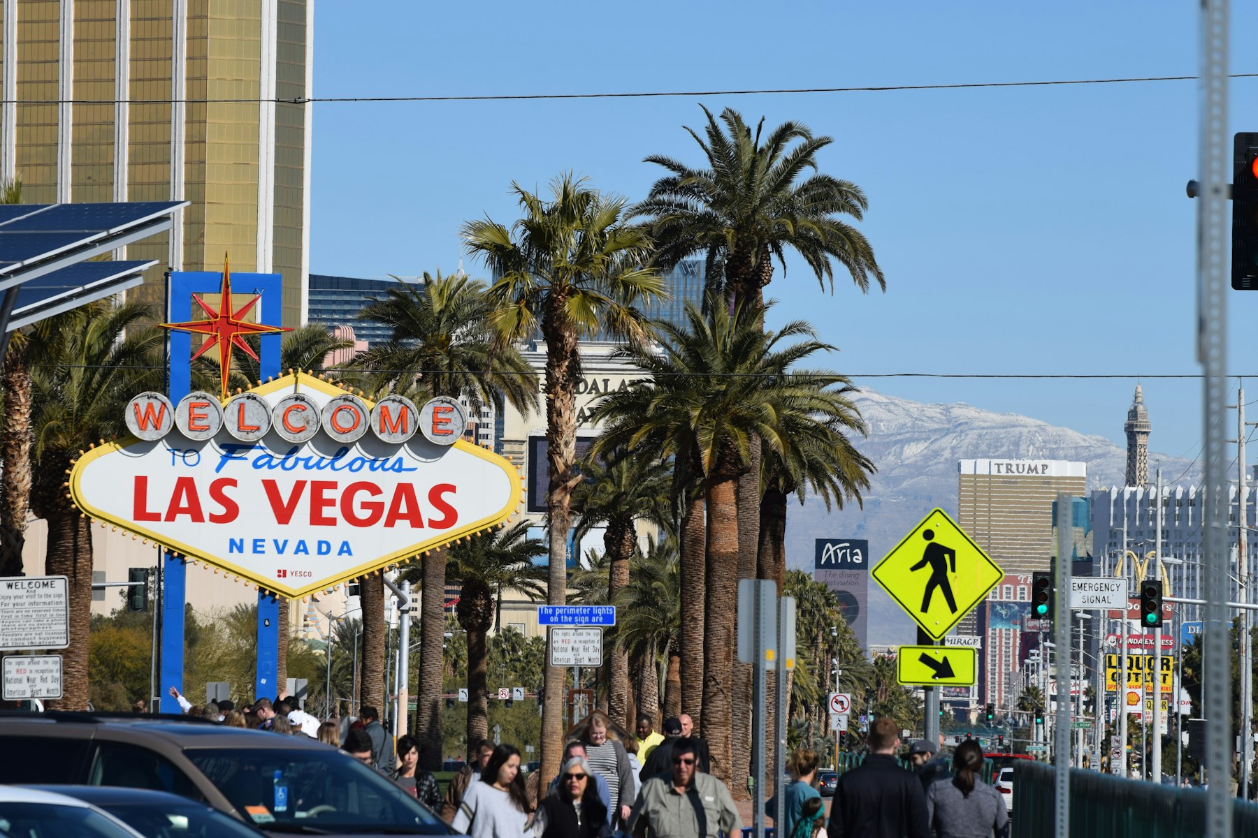 The Welcome to Fabulous Las Vegas sign beside palm trees with people crossing the road