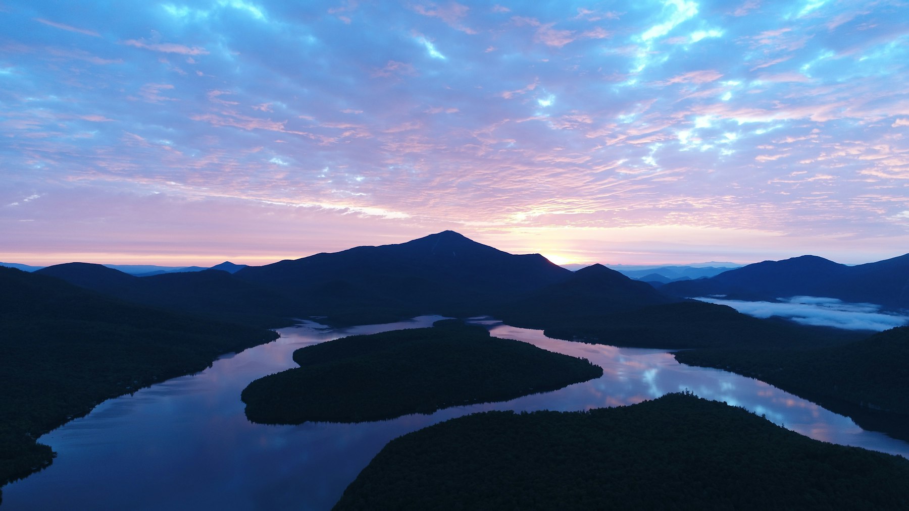 A lake with wooded islands and mountains behind it at sunset