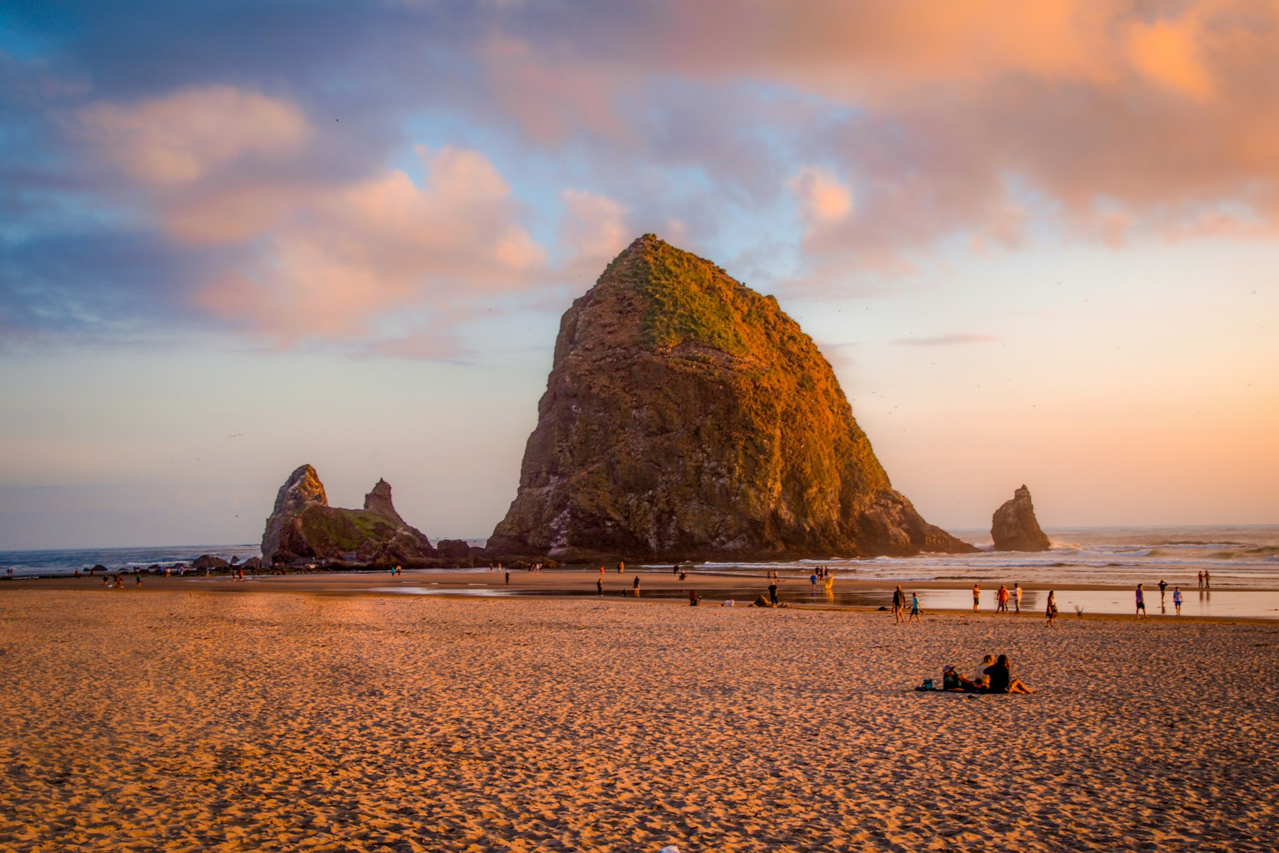 Haystack Rock at Cannon Beach Oregon at golden hour with people walking on the sand