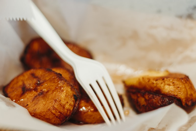 Fried pieces of plantain in a paper wrapper with a fork