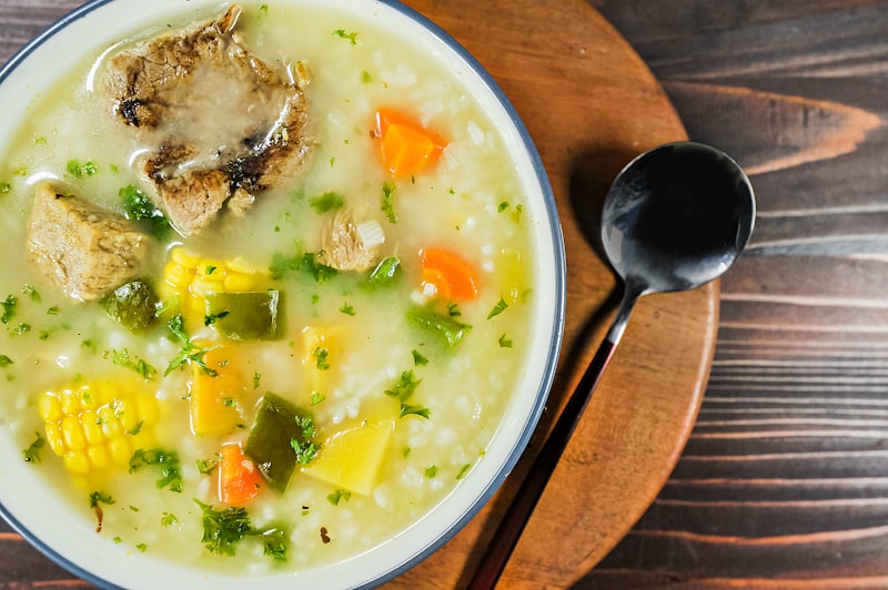 A bowl of soup with corn and vegetables and a spoon beside it