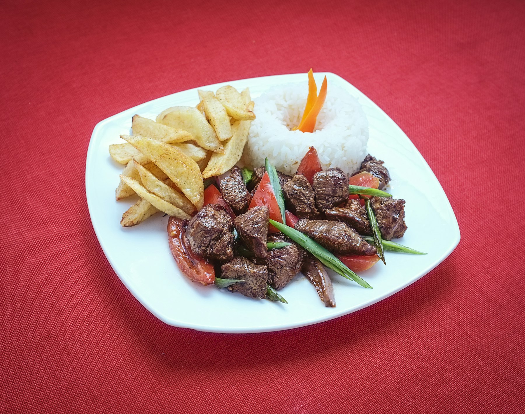 Lomo saltado with strips of beef tomato onion and french fries on a white plate
