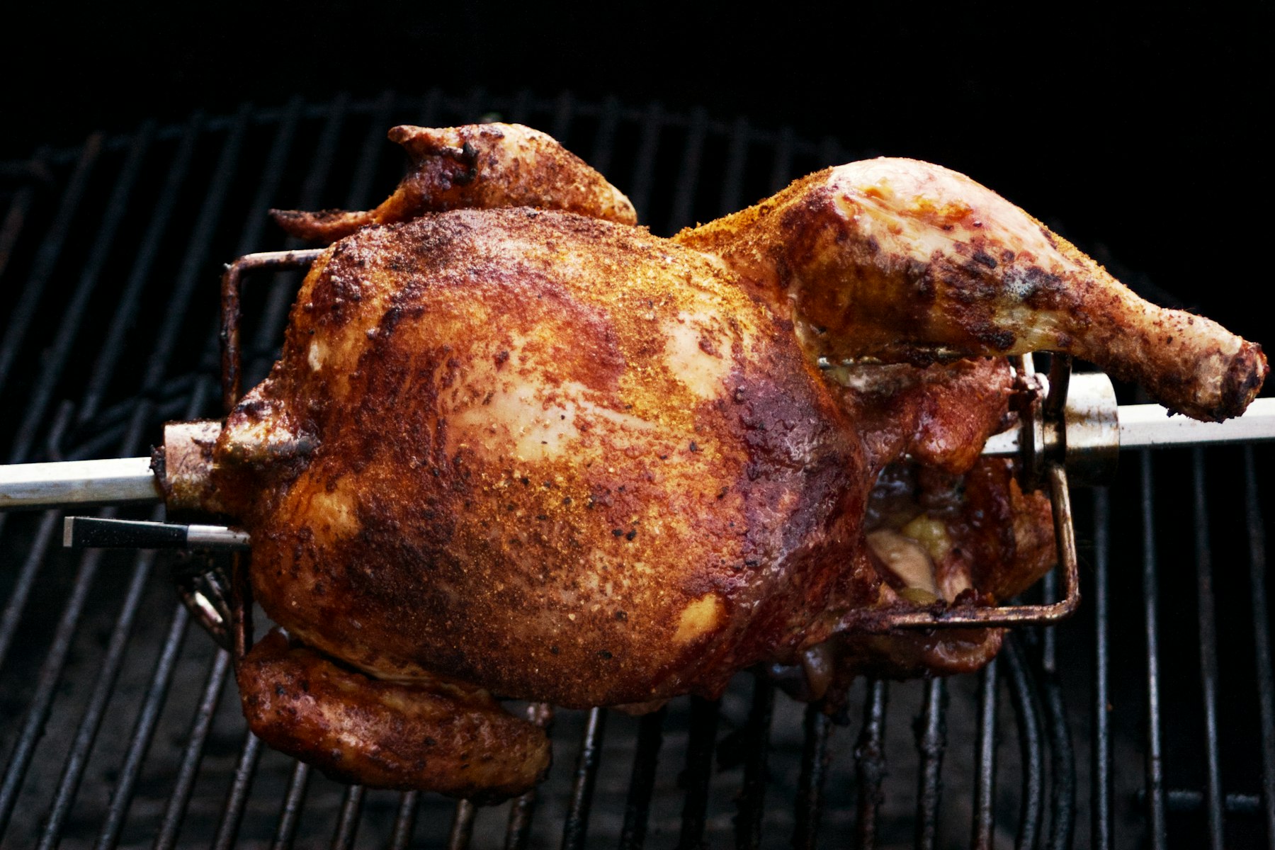 A whole chicken turning on a rotisserie spit over charcoal for pollo a la brasa