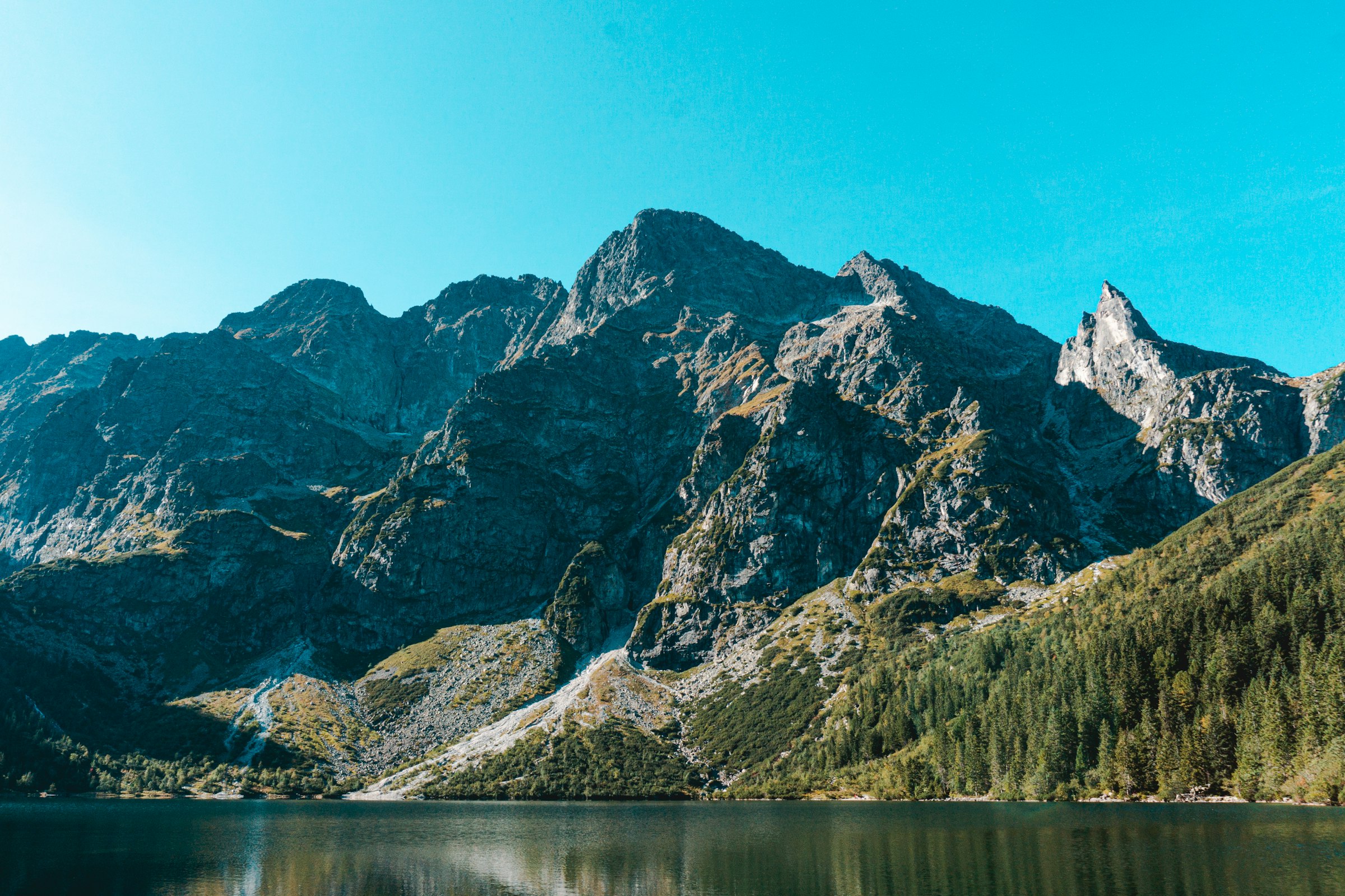 The grey peaks of the Tatra mountains rising above the still green water of Morskie Oko lake in southern Poland