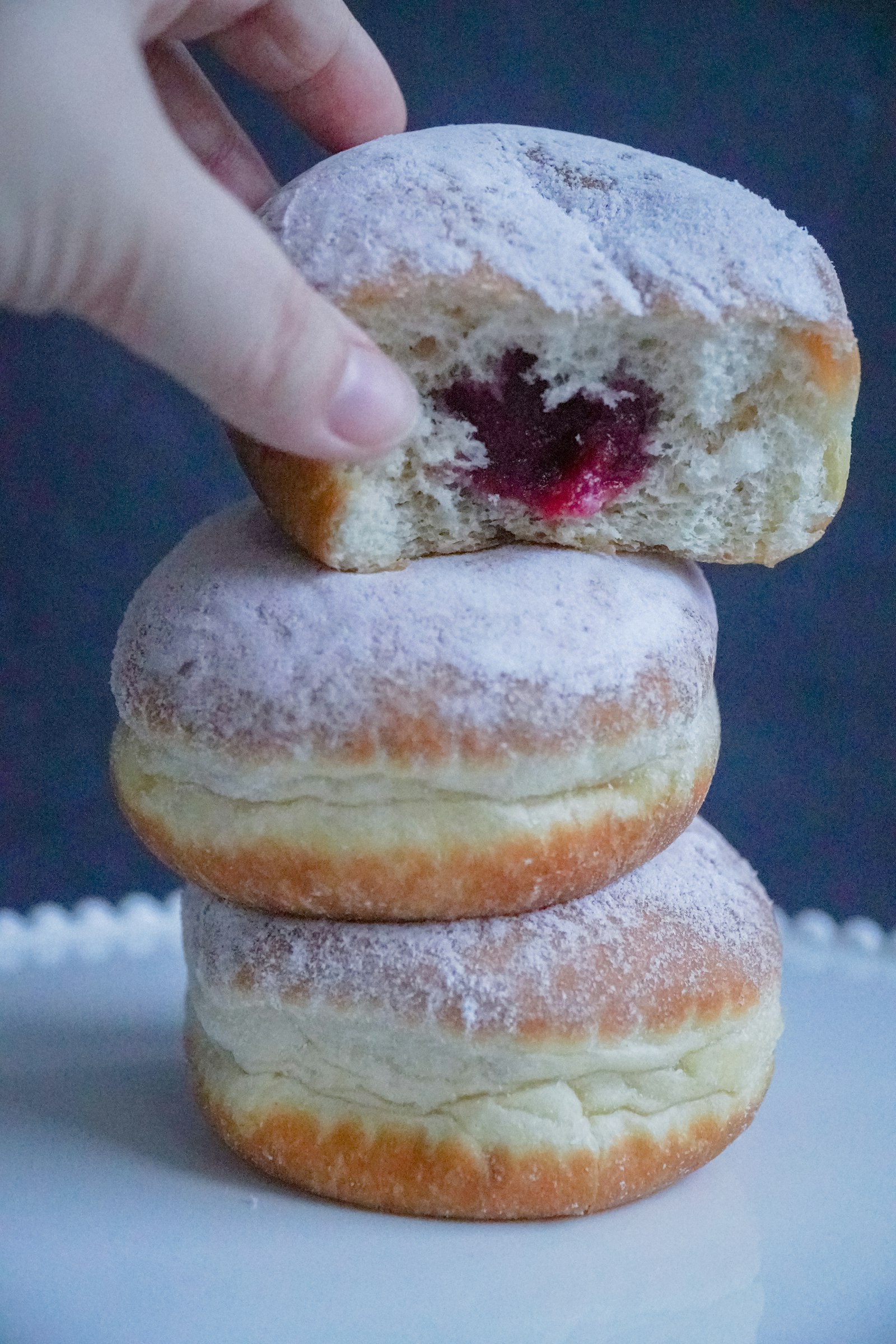 Sugar dusted Polish doughnuts stacked on a plate with jam filling showing