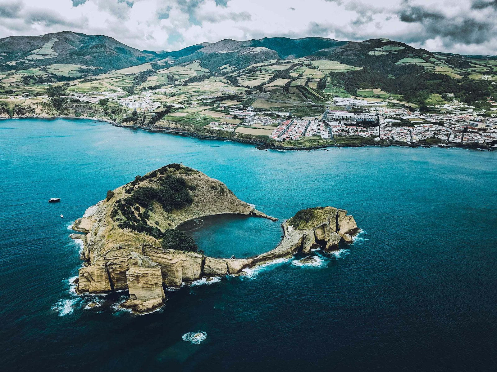 An aerial view of a green volcanic islet ringed by clear blue Atlantic water in the Azores