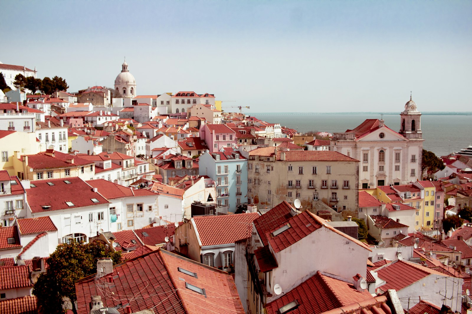 Red tiled rooftops of the Alfama district in Lisbon falling down toward the Tagus river
