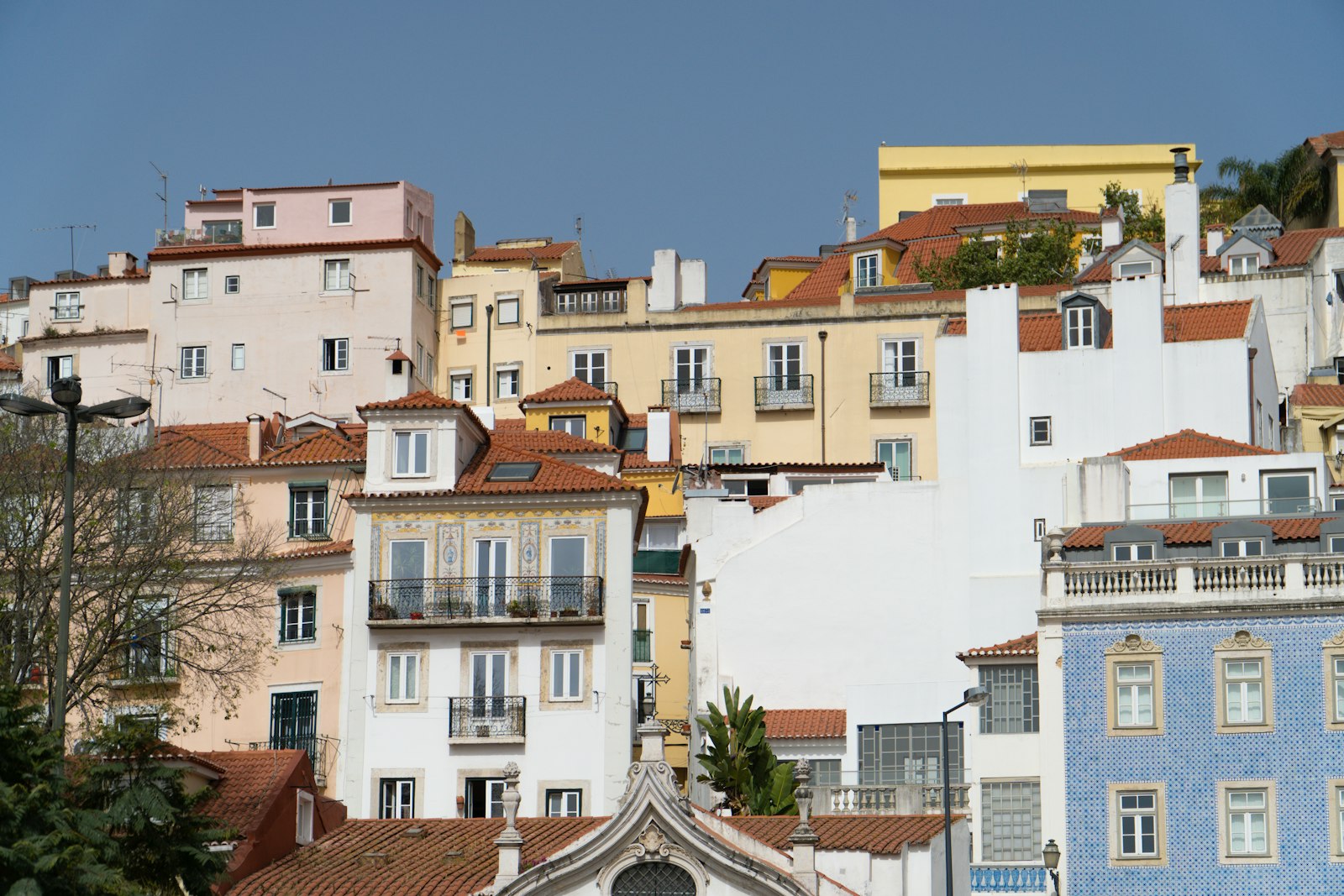 White and cream houses stacked up a Lisbon hillside with tiled facades and small balconies