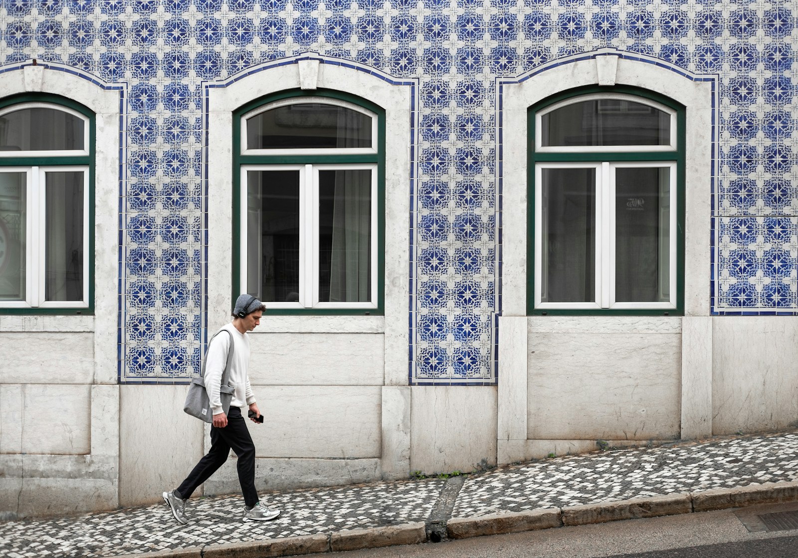 A man walking past an ordinary Lisbon building faced entirely in blue and white azulejo tiles