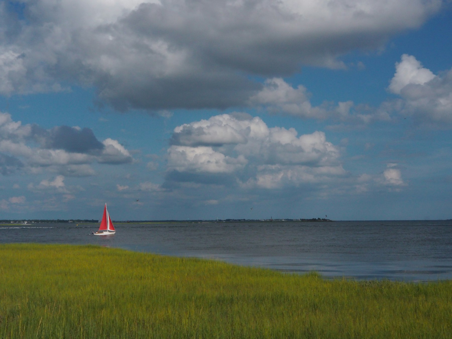 A small red sailboat on the water beyond the salt marsh near Charleston South Carolina