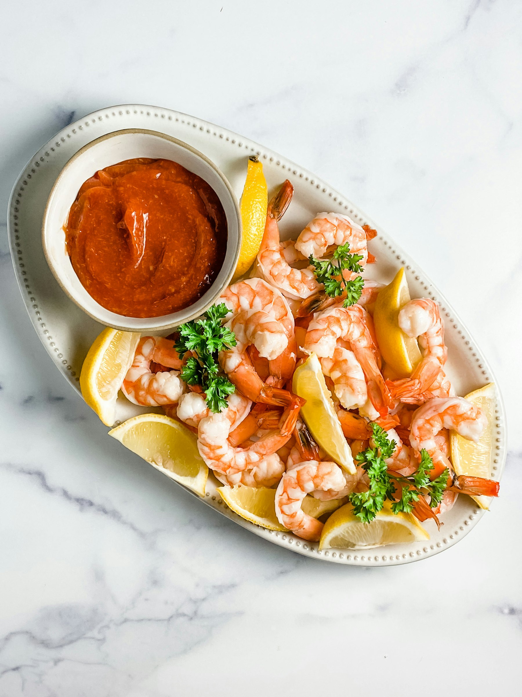 A plate of cooked shrimp with lemon wedges and cocktail sauce