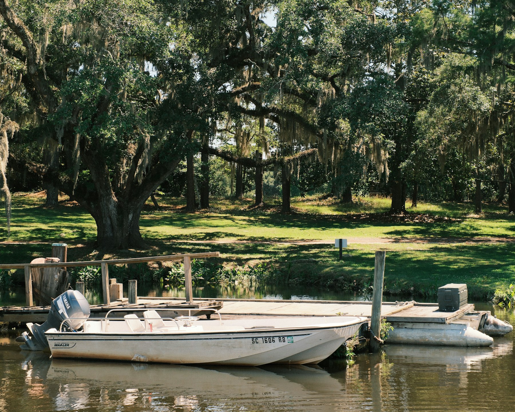 A small boat tied to a dock on calm water beneath moss draped live oaks in South Carolina