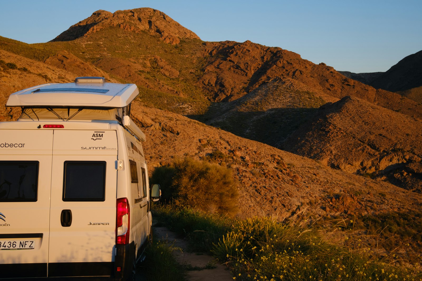 A white camper van parked on a dirt track below dry Spanish hills