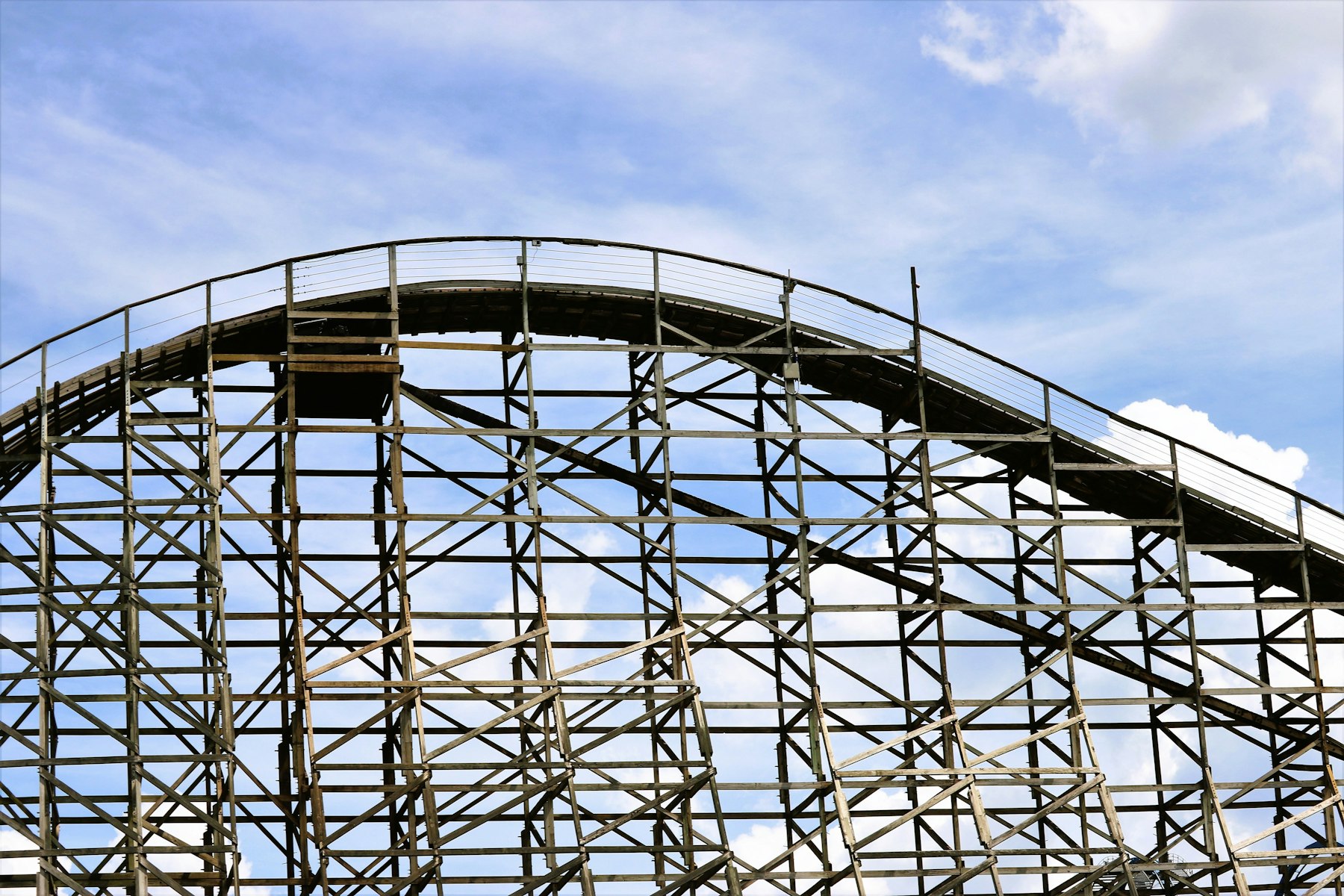 The timber structure of a wooden roller coaster against a blue sky