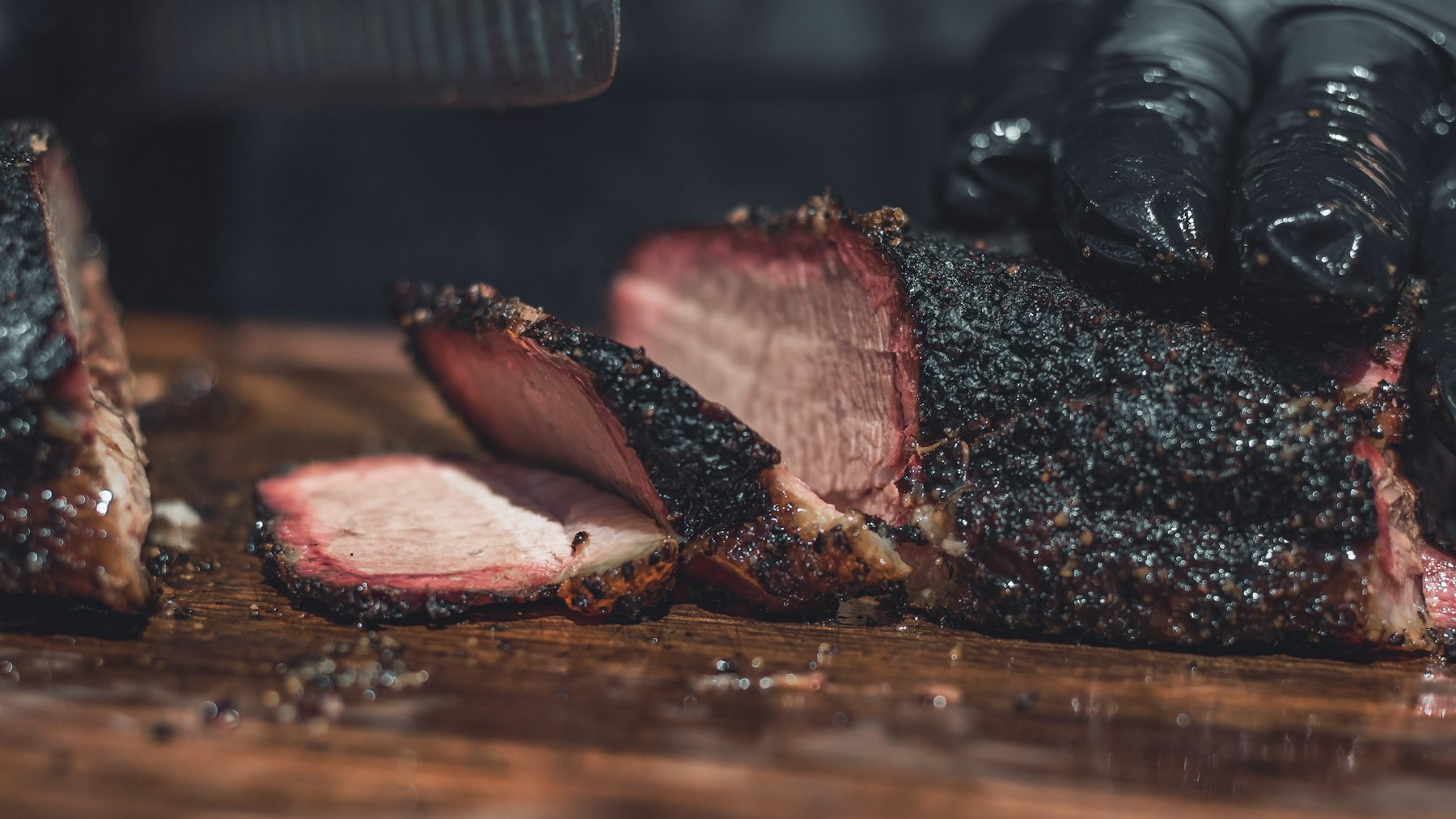 Sliced smoked brisket showing its dark bark and pink smoke ring on a wooden board