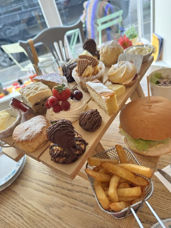 A tiered afternoon tea stand with scones, sandwiches, cakes and chips on a wooden table